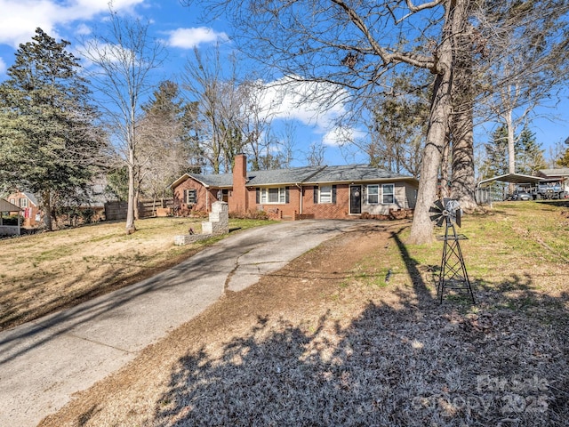 ranch-style house with driveway, brick siding, a chimney, and a front yard