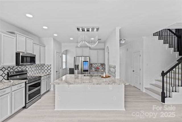 kitchen featuring sink, a center island with sink, light hardwood / wood-style flooring, appliances with stainless steel finishes, and light stone countertops