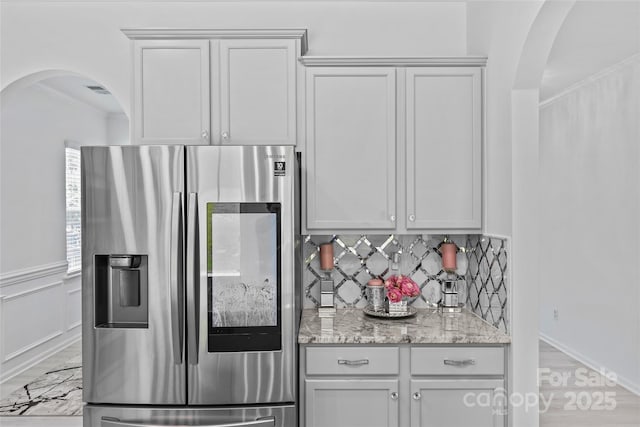 kitchen with stainless steel refrigerator with ice dispenser, crown molding, backsplash, light stone countertops, and white cabinets