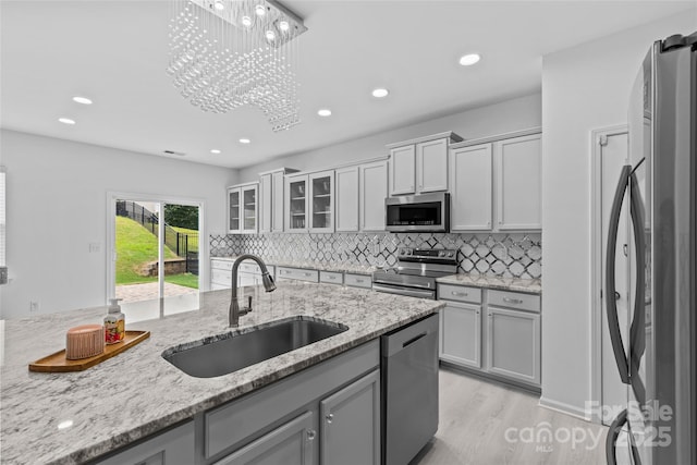 kitchen with light stone counters, stainless steel appliances, decorative light fixtures, and sink