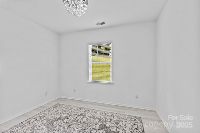 spare room featuring a chandelier and light wood-type flooring