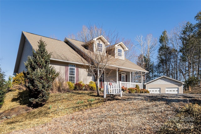 new england style home featuring covered porch, an outdoor structure, and a detached garage