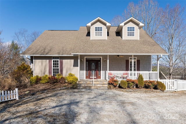 new england style home featuring covered porch, roof with shingles, and fence