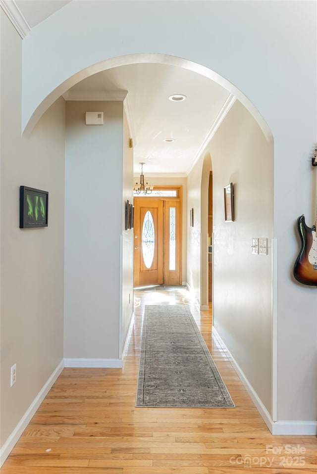 corridor with ornamental molding, light wood-style flooring, and baseboards