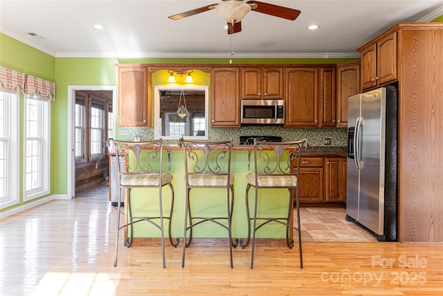 kitchen with appliances with stainless steel finishes, a breakfast bar, brown cabinets, and dark countertops