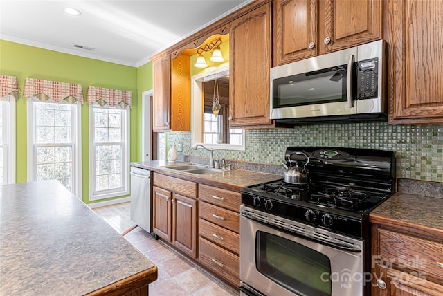 kitchen featuring brown cabinets, dark countertops, backsplash, appliances with stainless steel finishes, and a sink