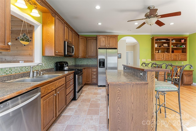 kitchen featuring dark countertops, a kitchen island, appliances with stainless steel finishes, a breakfast bar, and a sink