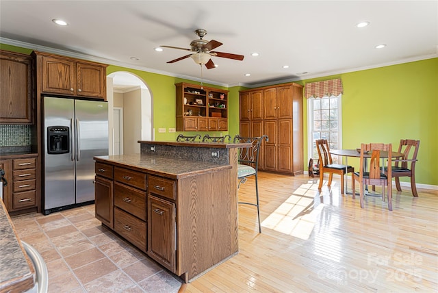 kitchen featuring a center island, arched walkways, dark stone countertops, stainless steel fridge, and a kitchen bar