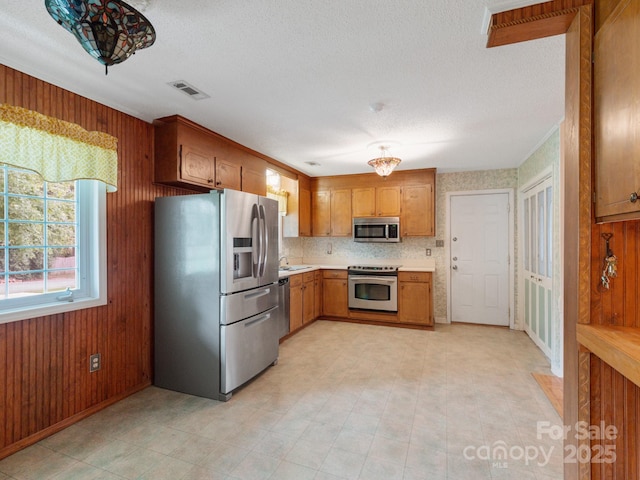 kitchen with wooden walls, stainless steel appliances, a sink, visible vents, and light countertops