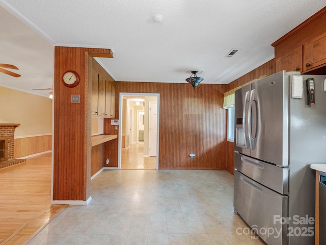 kitchen with wood walls, visible vents, open floor plan, a brick fireplace, and stainless steel fridge with ice dispenser