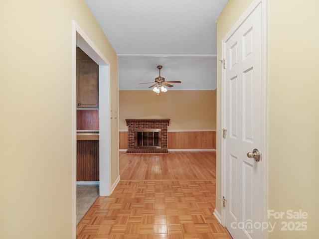 corridor featuring wooden walls, wainscoting, and a textured ceiling