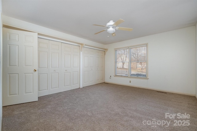 unfurnished bedroom with ceiling fan, two closets, and light colored carpet