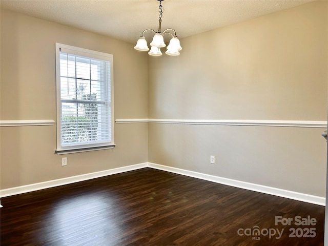 spare room featuring baseboards, dark wood-type flooring, a notable chandelier, and a textured ceiling