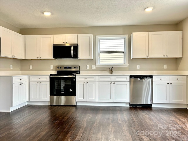 kitchen featuring light countertops, appliances with stainless steel finishes, dark wood-style floors, white cabinets, and a sink