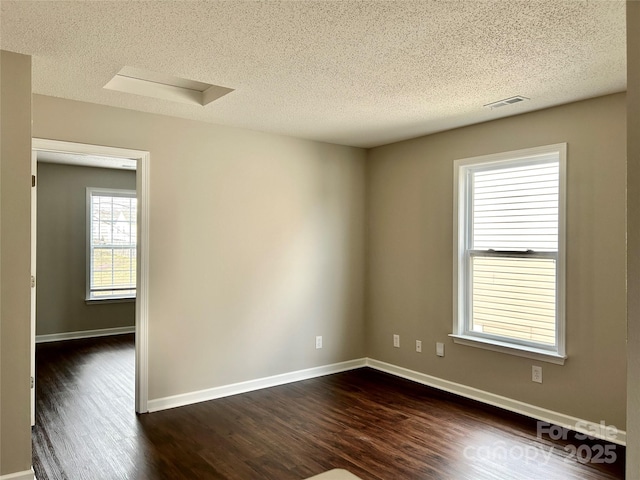 empty room with visible vents, baseboards, dark wood-type flooring, and a textured ceiling