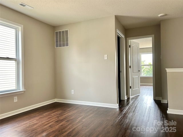 spare room featuring dark wood-style floors, visible vents, a textured ceiling, and baseboards