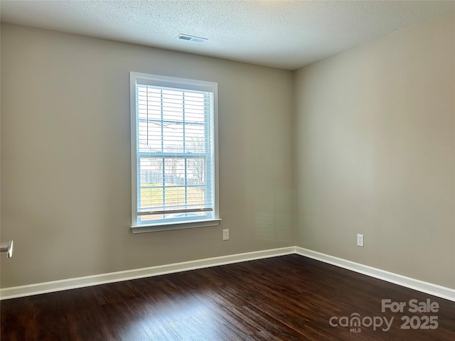 empty room with visible vents, a textured ceiling, dark wood-type flooring, and baseboards