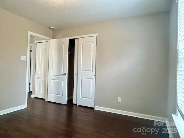 unfurnished bedroom featuring a closet, baseboards, and dark wood-style flooring