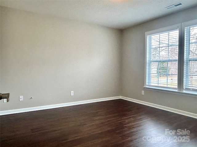 spare room featuring visible vents, baseboards, a textured ceiling, and dark wood finished floors