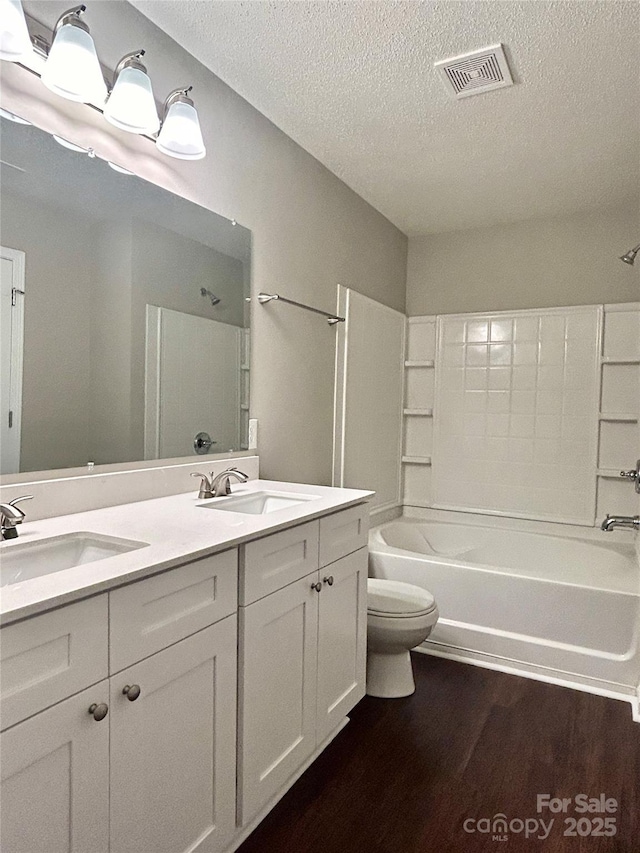 bathroom featuring toilet, wood finished floors, visible vents, and a sink