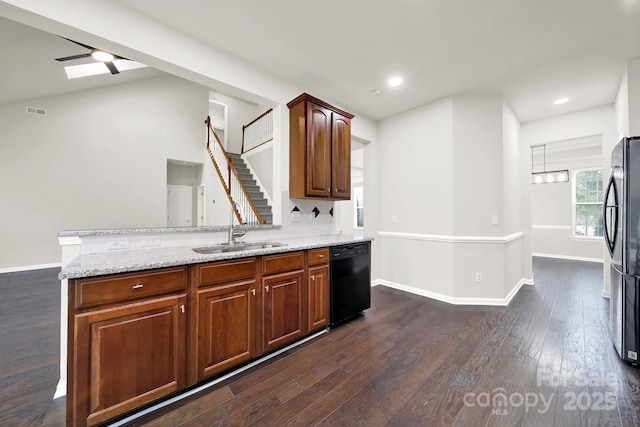 kitchen featuring black dishwasher, light stone counters, freestanding refrigerator, dark wood-style floors, and a sink