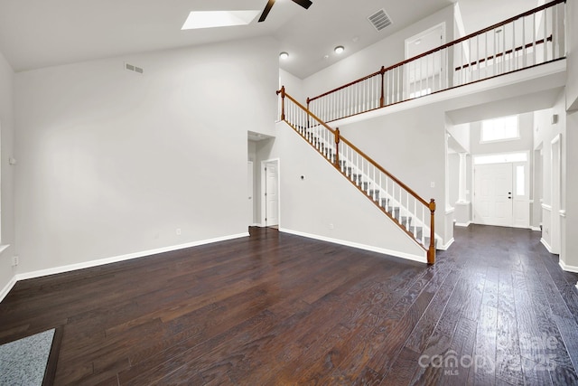 unfurnished living room with visible vents, a ceiling fan, hardwood / wood-style flooring, stairway, and a skylight