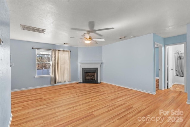unfurnished living room with a fireplace with flush hearth, light wood-style flooring, visible vents, and baseboards