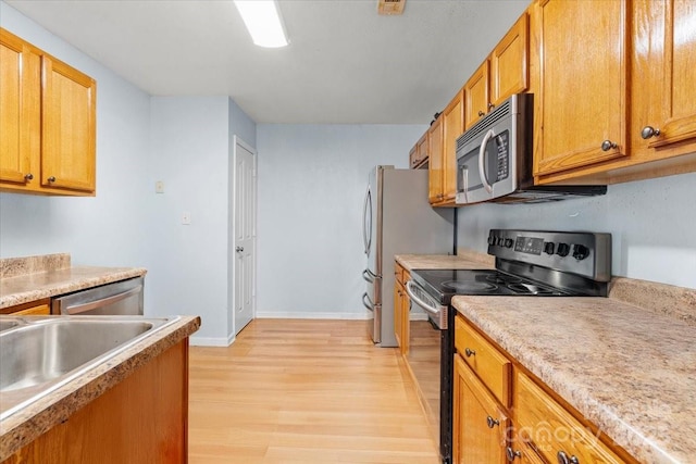 kitchen with brown cabinets, stainless steel appliances, light countertops, light wood-type flooring, and baseboards