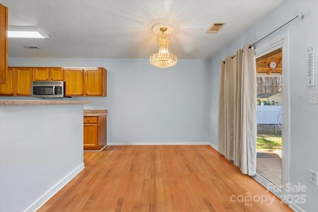 kitchen featuring brown cabinets, light wood finished floors, stainless steel microwave, a notable chandelier, and visible vents