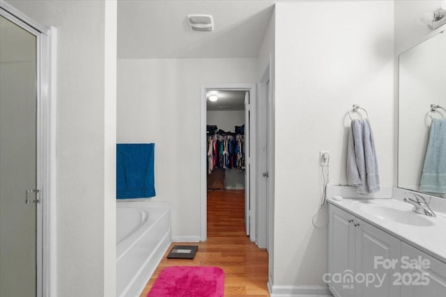bathroom featuring baseboards, wood finished floors, a garden tub, vanity, and a walk in closet