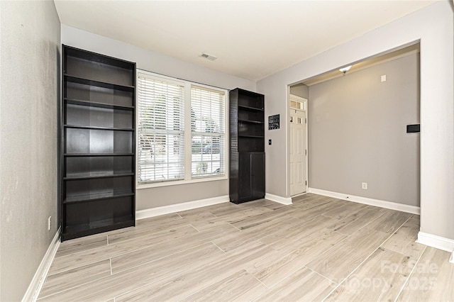 empty room with light wood-style flooring, visible vents, and baseboards