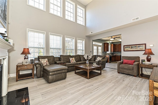 living area with a fireplace with flush hearth, visible vents, light wood finished floors, and a ceiling fan