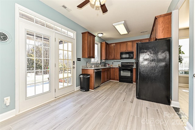 kitchen featuring visible vents, light wood-style floors, brown cabinets, black appliances, and a sink