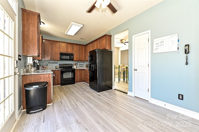 kitchen featuring a ceiling fan, brown cabinetry, a sink, light stone countertops, and black appliances