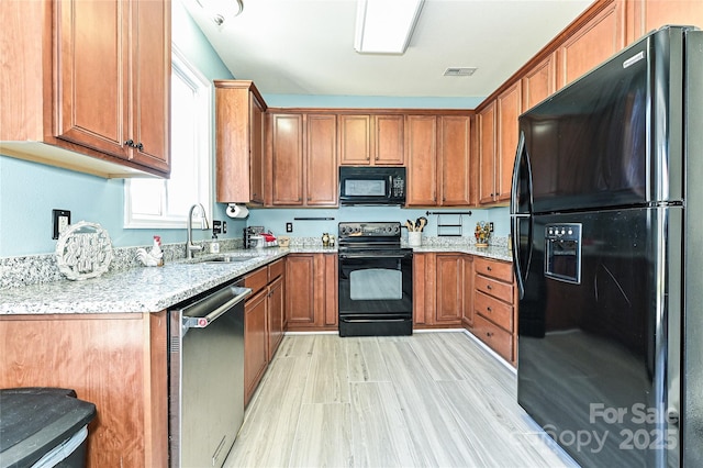 kitchen featuring light stone counters, brown cabinets, visible vents, a sink, and black appliances