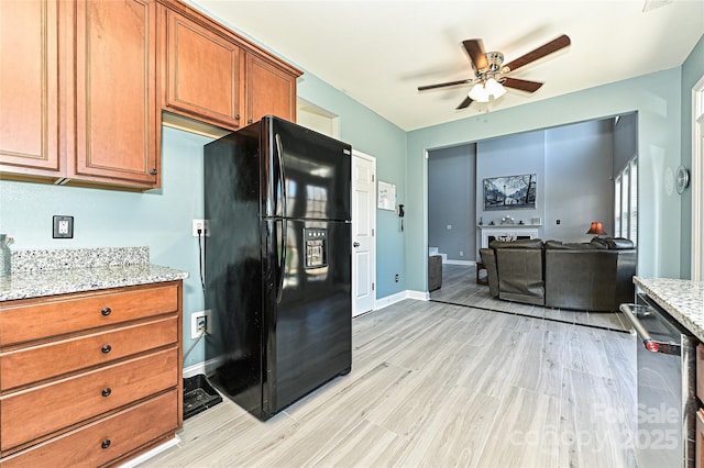 kitchen featuring brown cabinetry, freestanding refrigerator, stainless steel dishwasher, and light stone countertops