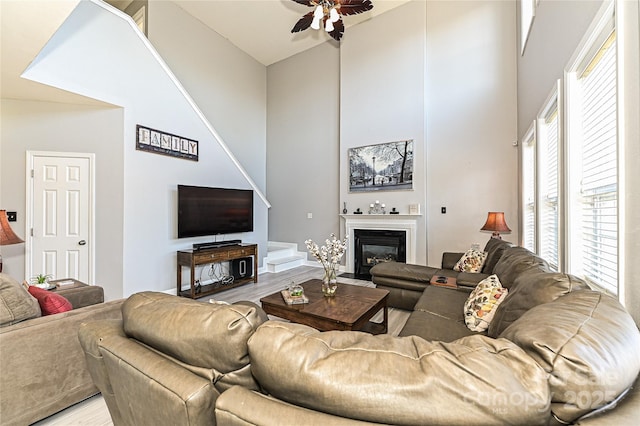 living area with a fireplace with flush hearth, ceiling fan, a towering ceiling, and wood finished floors