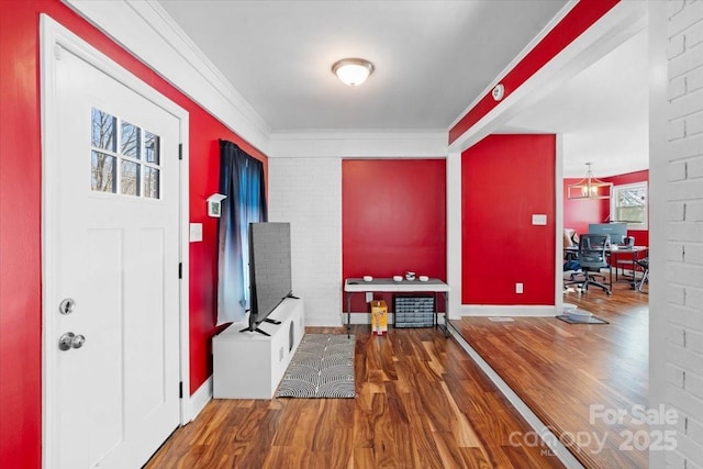 foyer entrance featuring hardwood / wood-style flooring, crown molding, and brick wall