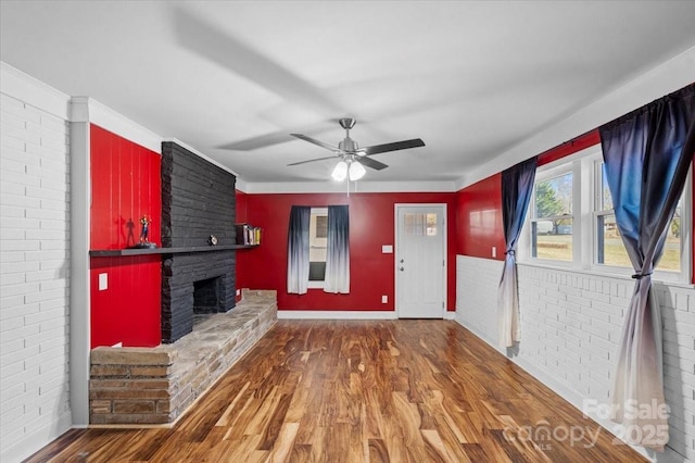 unfurnished living room featuring dark wood-type flooring, a large fireplace, brick wall, and ceiling fan