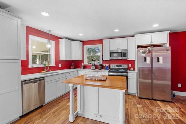 kitchen with white cabinetry, sink, hanging light fixtures, stainless steel appliances, and light wood-type flooring