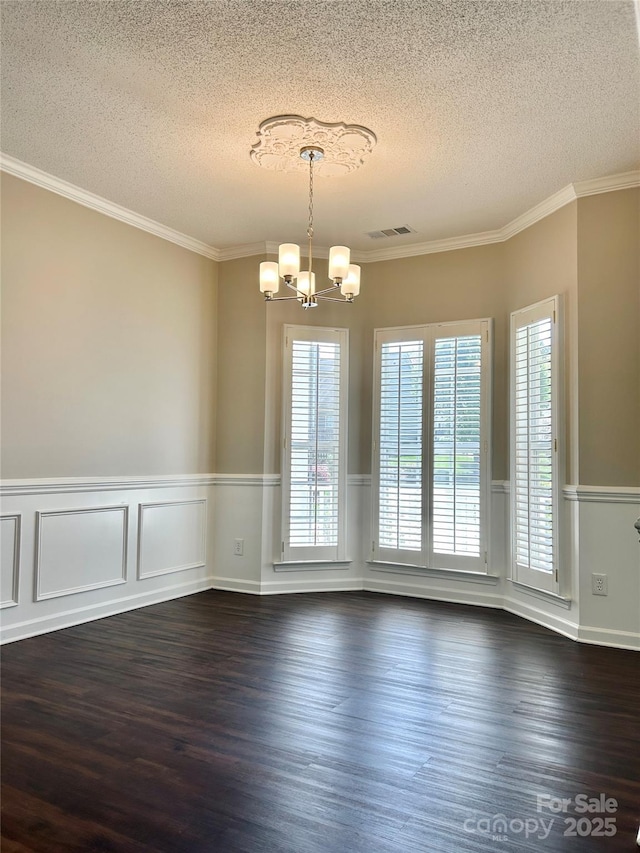 unfurnished room with a chandelier, dark wood finished floors, a textured ceiling, a wainscoted wall, and visible vents