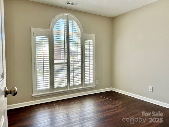unfurnished room with dark wood-type flooring, a wealth of natural light, and visible vents