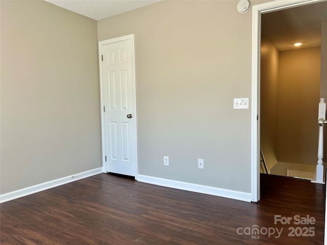 unfurnished room featuring baseboards and dark wood-type flooring