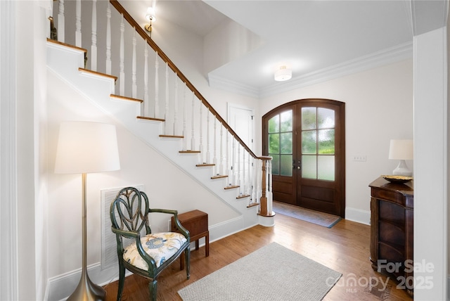 entryway featuring arched walkways, french doors, crown molding, stairway, and wood finished floors