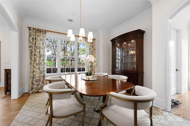 dining space featuring light wood-type flooring, an inviting chandelier, baseboards, and crown molding