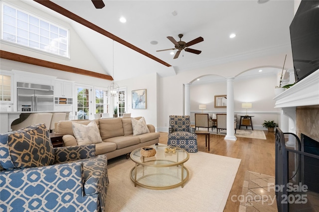 living room featuring a ceiling fan, decorative columns, light wood-style flooring, and high vaulted ceiling