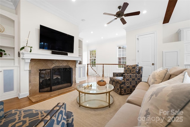 living room with wood finished floors, crown molding, built in shelves, a fireplace, and recessed lighting