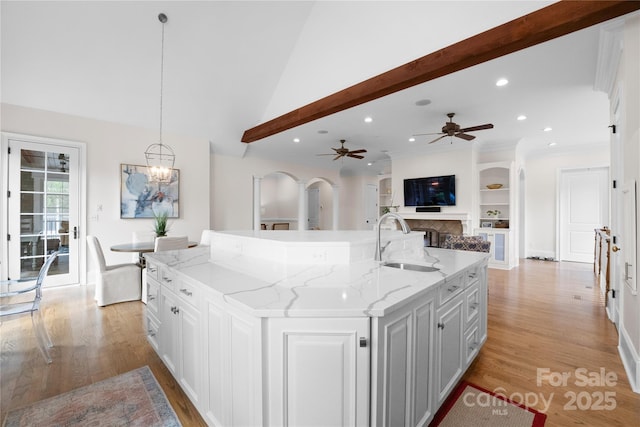 kitchen with arched walkways, white cabinetry, a sink, an island with sink, and light wood-type flooring