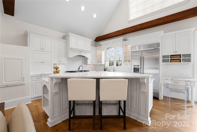 kitchen with light countertops, a kitchen bar, built in fridge, and white cabinetry