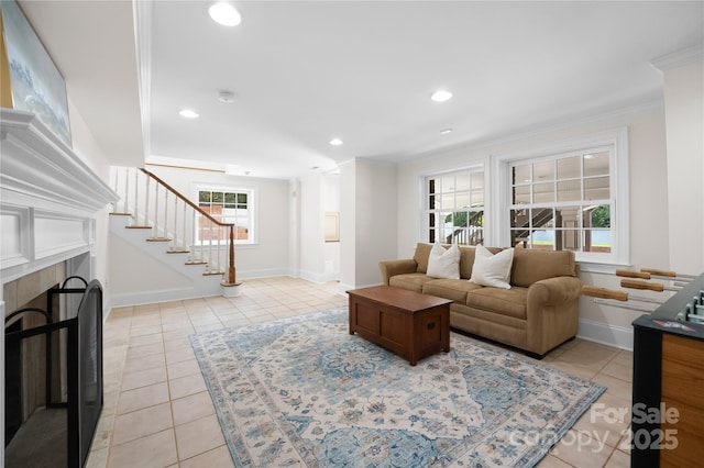 living room with crown molding, light tile patterned floors, a tile fireplace, baseboards, and stairs